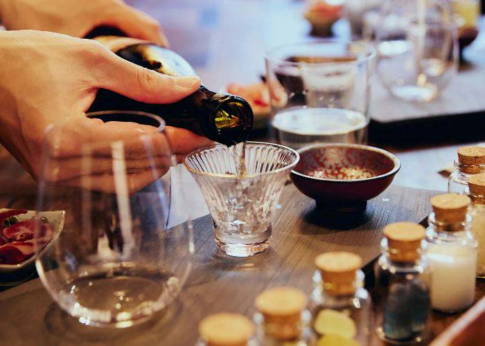 A cup of sake being delicately poured, surrounded by other glasses and spices.